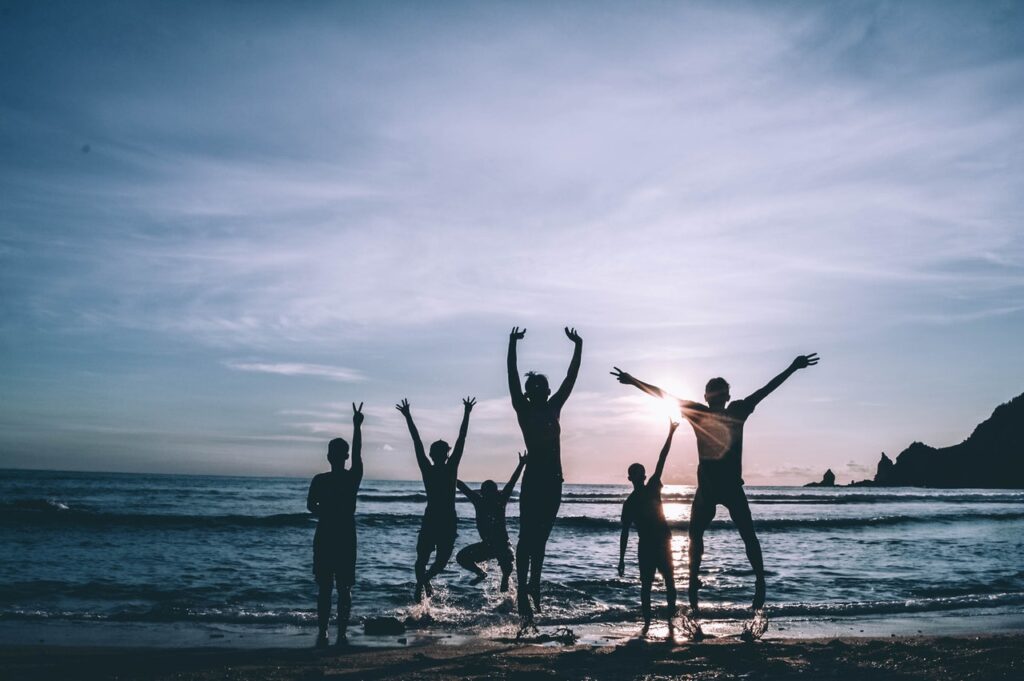 People jumping in front of water and a sunset